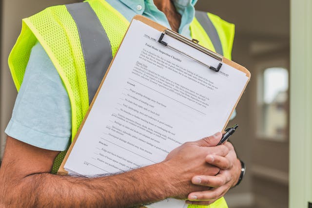 Person wearing a yellow safety vest, holding a clipboard with a home inspection checklist